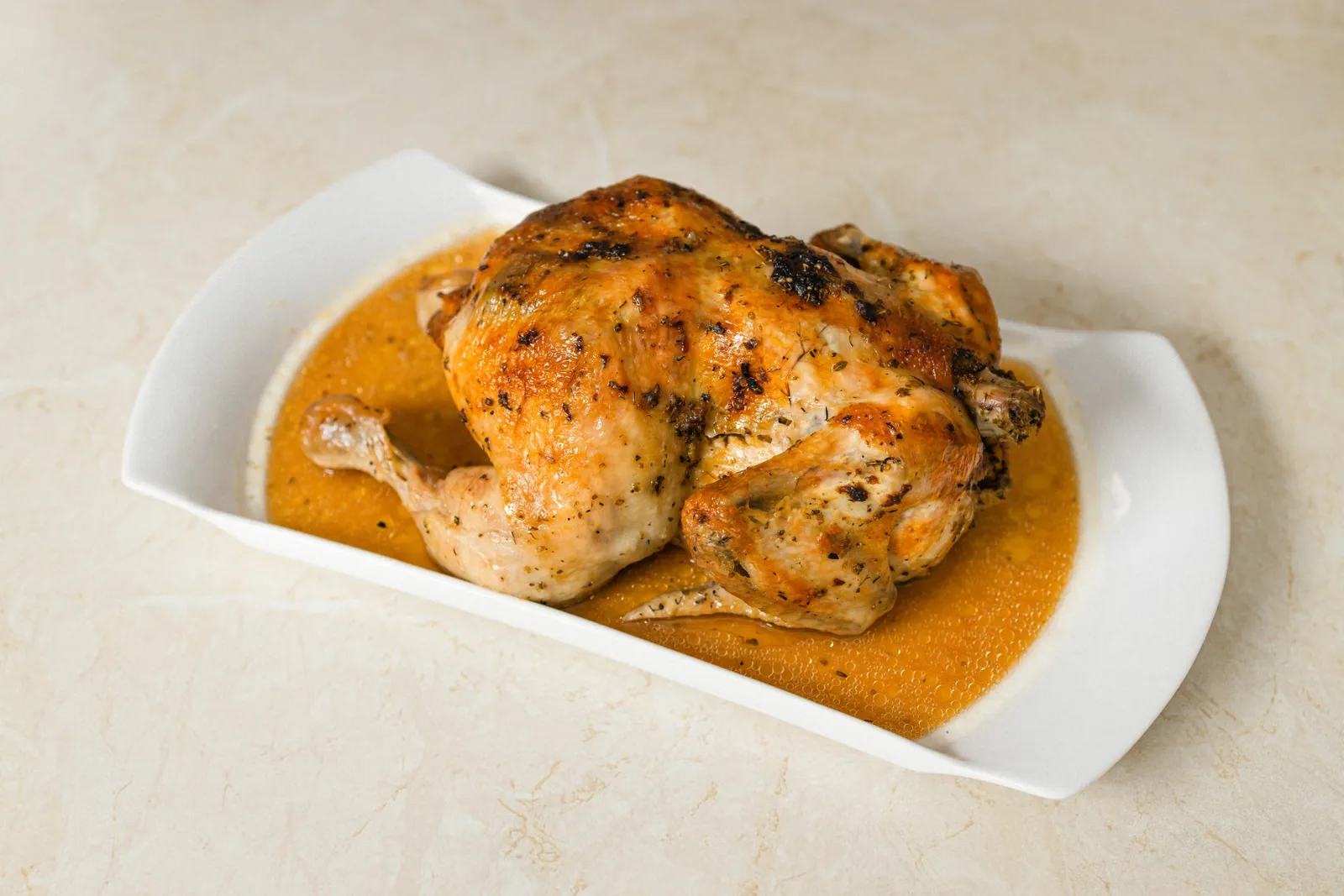 Volaille rôtie entière à la peau dorée, servie sur un plat blanc avec sa sauce